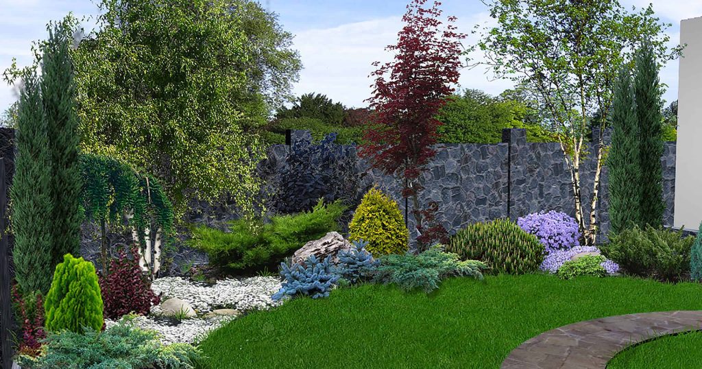 A lush garden features a variety of plants and trees, including tall evergreens, deciduous trees, and colorful shrubs. A stone pathway curves through the green lawn, leading to a backdrop of a gray stone wall with trees in the background—perfectly complemented by expert masonry services Connecticut.
